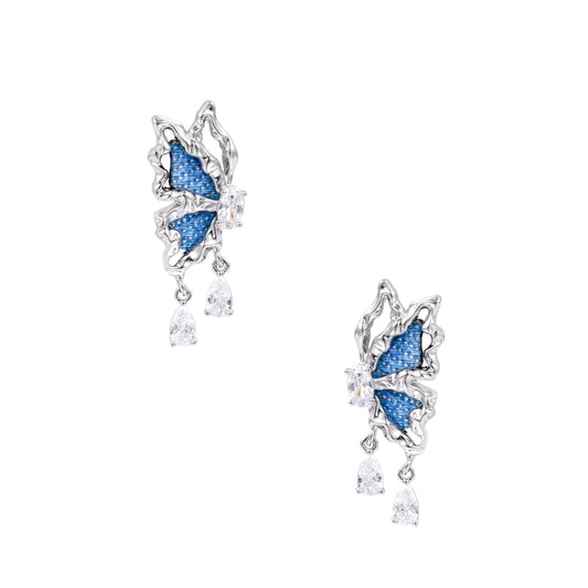 Silver butterfly earrings with blue denim fabric wings and dangling teardrop crystals on cream background