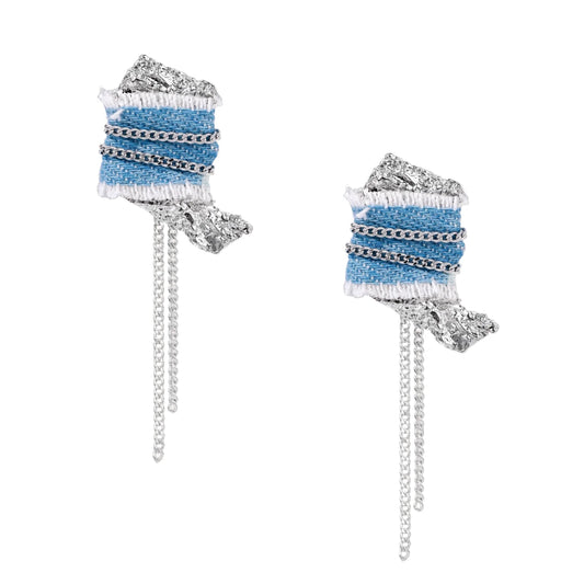 Blue denim fabric earrings with white fringe, silver chains, metallic accents, and dangling chain tassels on cream background.