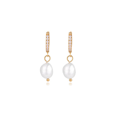 Gold huggie hoop earrings with pavé crystals and white freshwater pearl drops on cream background