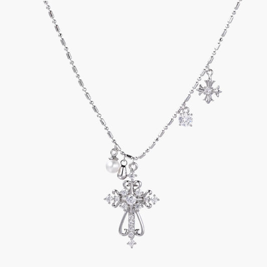 Ornate white gold-plated cross pendant with zirconia stones and pearl accents on adjustable silver chain against cream background