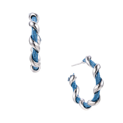 White gold-plated hoops intertwined with blue denim fabric in a twisted rope design on cream background.