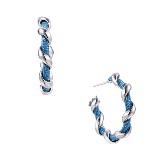 White gold-plated hoops intertwined with blue denim fabric in a twisted rope design on cream background.