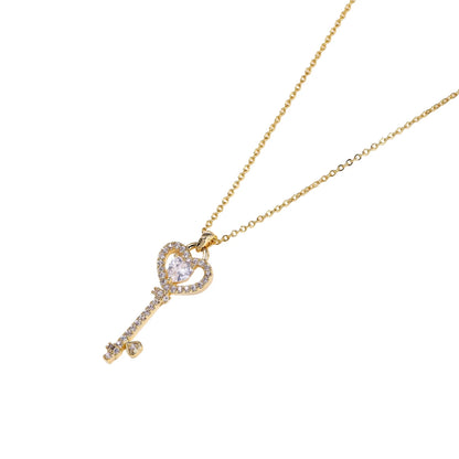 Delicate gold key pendant with heart-shaped bow and crystal pavé detailing on fine chain against cream background.
