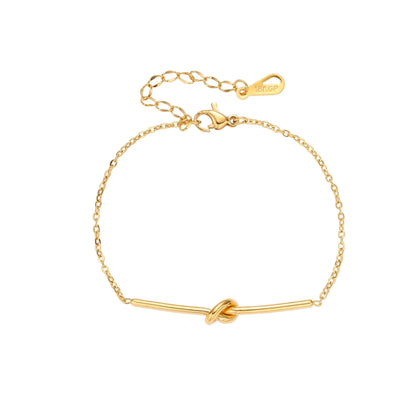 Delicate gold chain bracelet with minimalist bar and centered knot detail on cream background