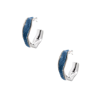 Silver huggie hoops with blue denim fabric inlay strip and polished white gold plated finish on cream background.