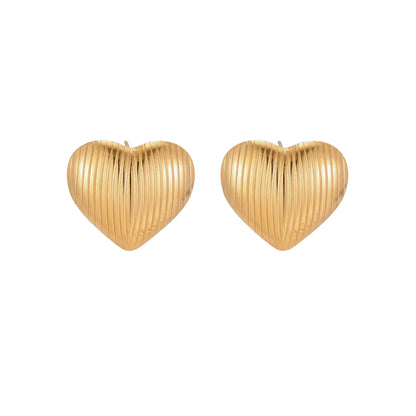 Gold heart-shaped stud earrings with parallel ridged texture on cream background