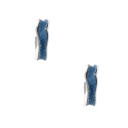 Silver huggie hoops with blue denim fabric inlay strip and polished white gold plated finish on cream background.