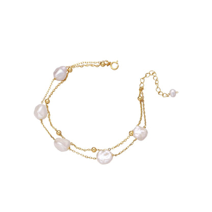 Double-strand gold bracelet with irregular baroque pearls and smooth freshwater pearls on cream background.