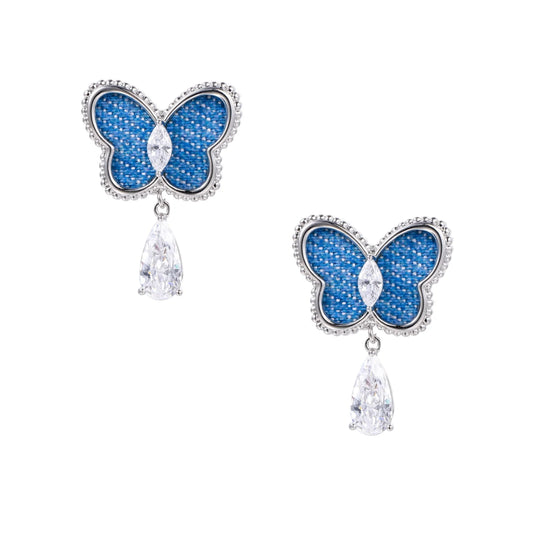 Blue denim butterfly earrings with silver frame and teardrop crystal dangles on cream background