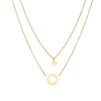 Gold layered necklace set with sunburst and smiley face pendants on delicate chains against white background.