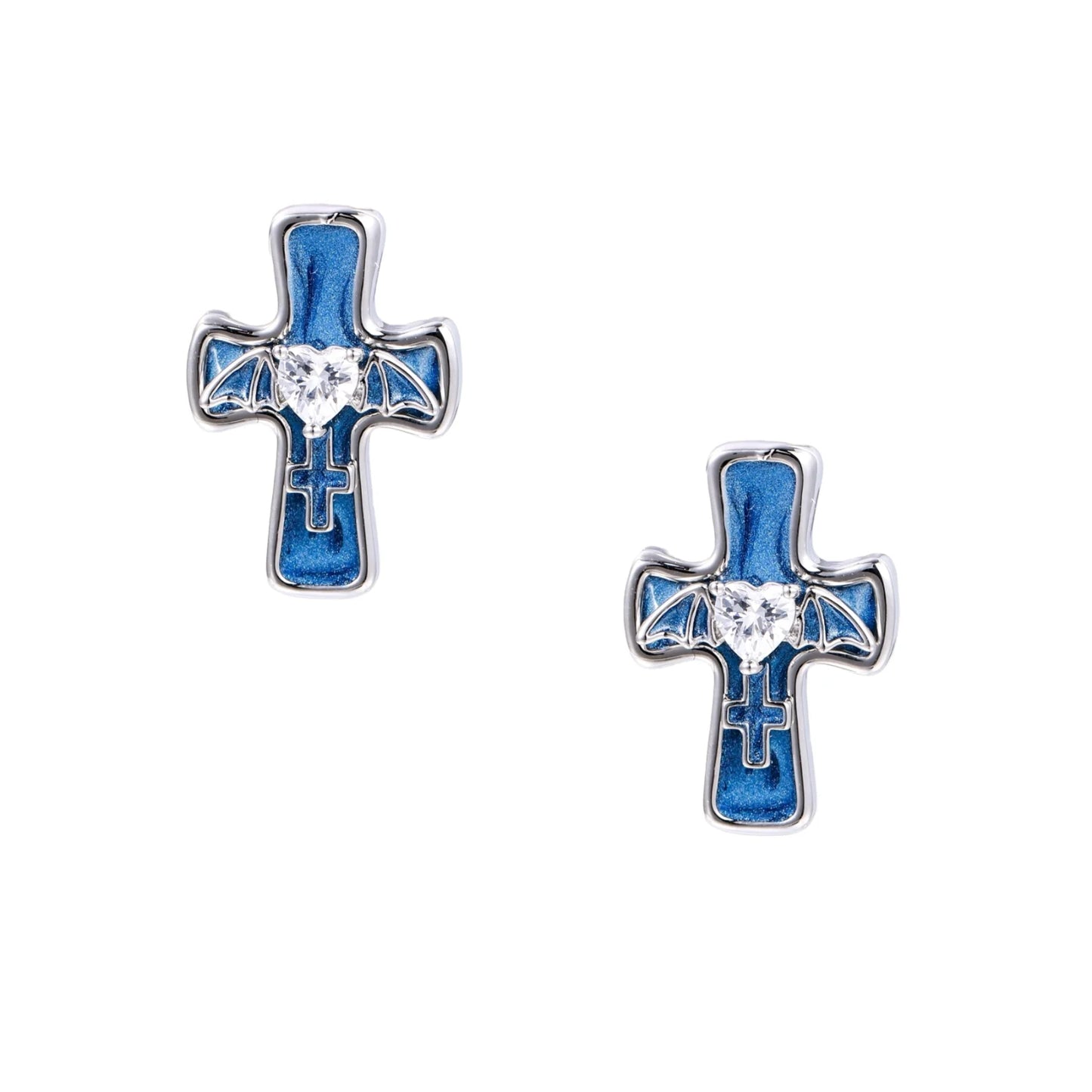 White gold-plated cross earrings with blue enamel, bat wing details, and heart-shaped zirconia center on cream background.