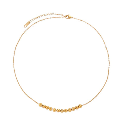 Delicate gold-plated necklace with graduated spherical beads forming gentle smile curve on beige background
