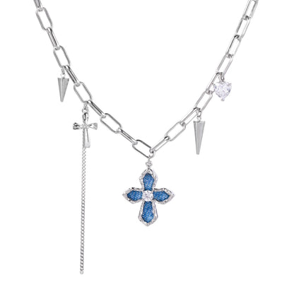White gold plated chain necklace with blue textured cross pendant, spike charms, and mini cross detail on beige background