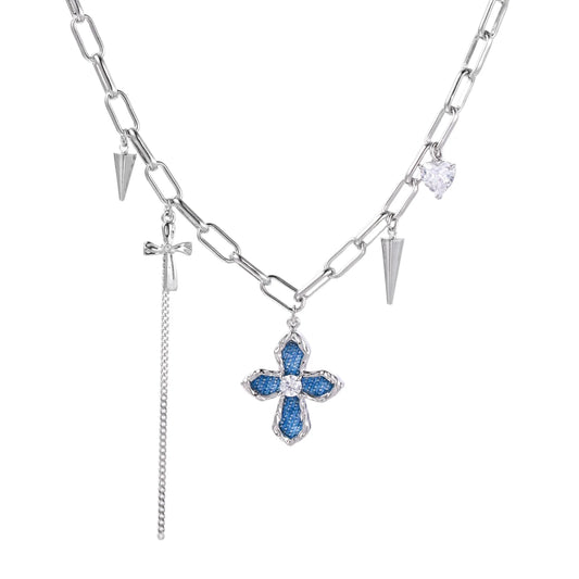 White gold plated chain necklace with blue textured cross pendant, spike charms, and mini cross detail on beige background
