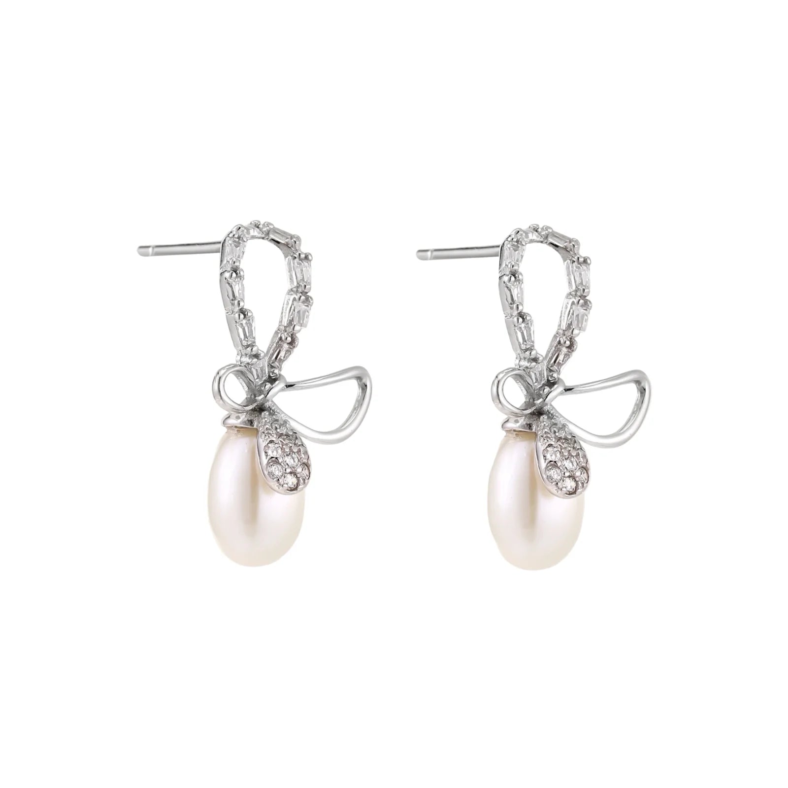 Silver bow-shaped stud earrings with baguette crystals and dangling white freshwater pearls on cream background