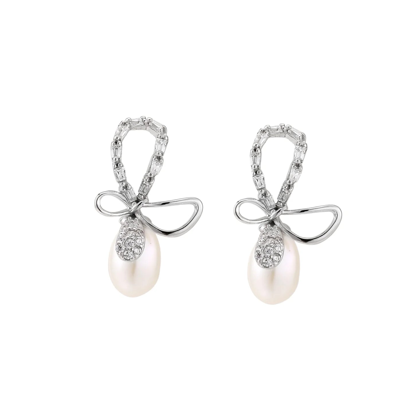 Silver bow-shaped stud earrings with baguette crystals and dangling white freshwater pearls on cream background