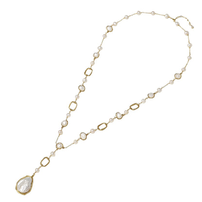 Y-shaped gold necklace with alternating geometric links, freshwater pearls, and baroque pearl pendant on cream background